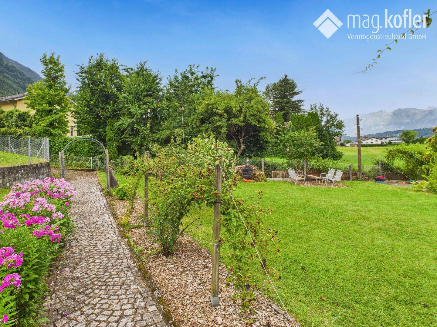Blühender Gartenweg führt zu einer Rasenfläche mit Sitzgelegenheiten und Weitblick.