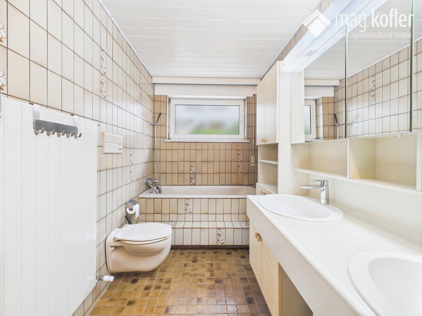 Badezimmer mit Badewanne, WC, Doppelwaschbecken und Fliesen im 80er-Jahre-Stil.