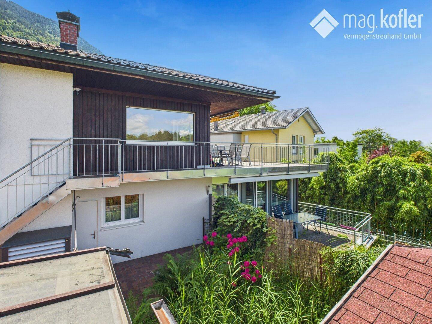 Mehrstöckiges Haus mit mehreren Terrassen und Balkonen, umgeben von viel Grün.