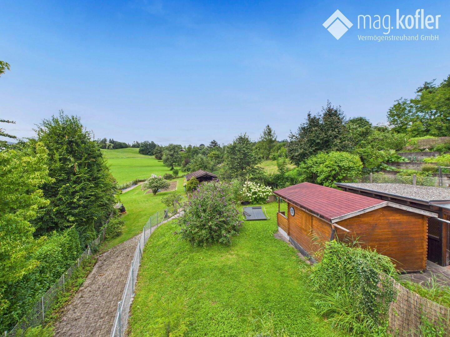 Panoramablick über den weitläufigen Garten mit mehreren Holzgebäuden und viel Grün.