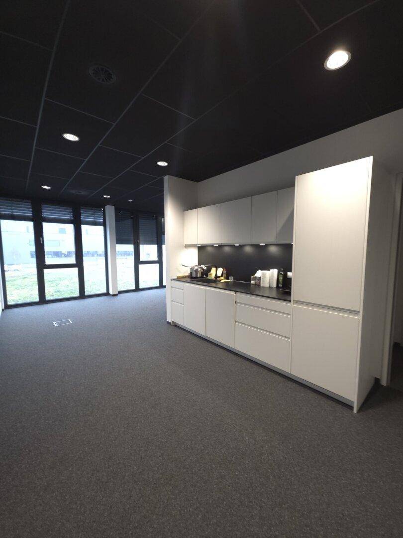 Moderne Teeküche in einem Büroraum mit weißen Schränken und dunkler Decke.