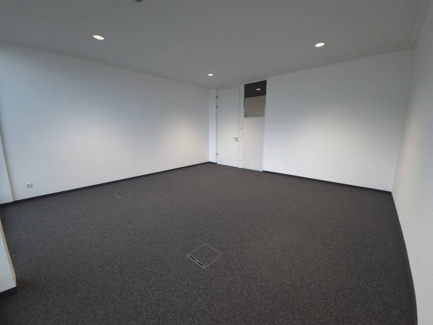 Heller Büroraum mit Teppichboden und weißen Wänden, ideal für flexible Arbeitsplatzgestaltung.