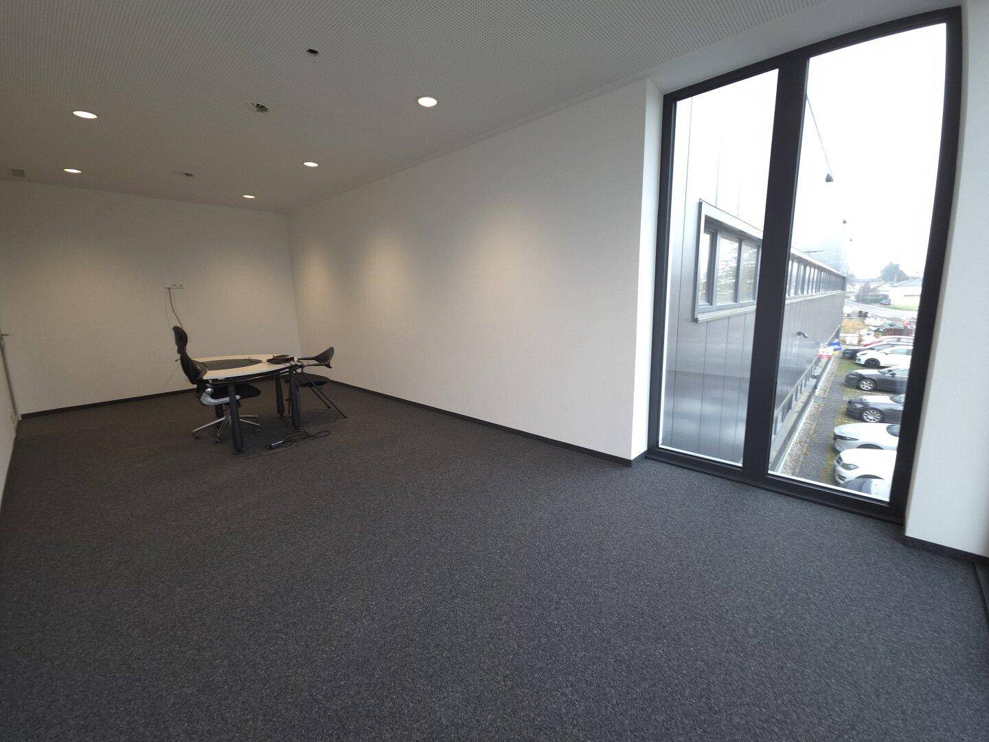 Büroraum mit Schreibtisch und Blick auf den Parkplatz durch große Fenster.