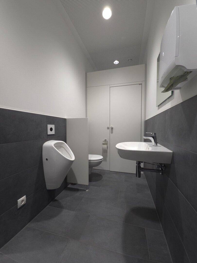 Modernes WC mit Urinal, dunklen Fliesen und weißer Keramik, sehr gepflegt.