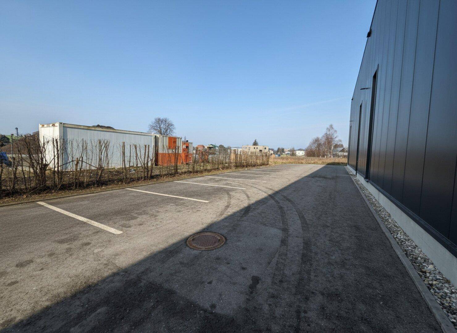 Großer Außenparkplatz neben dem modernen Geschäftsgebäude unter blauem Himmel.