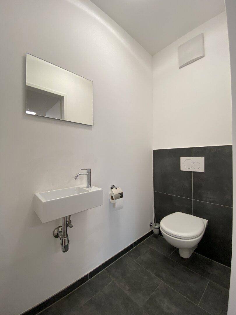 Modernes Gäste-WC mit wandhängendem WC, kleinem Waschbecken und dunklen Fliesen.