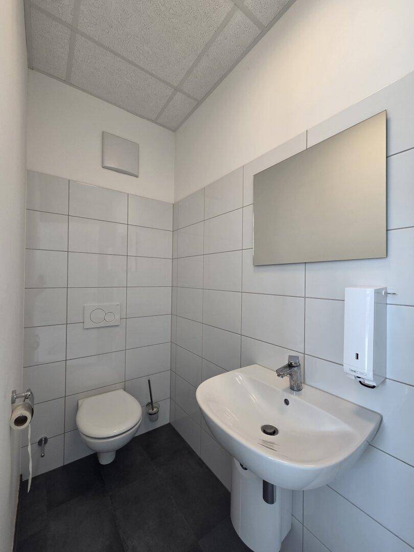 Saubere und funktionale Toilette mit Waschbecken, Wand-WC und hellen Fliesen.