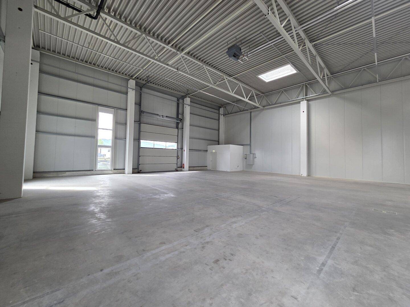 Moderne Lagerhalle mit Betonboden, hohen Decken und einem Rolltor, bereit zur Einrichtung.
