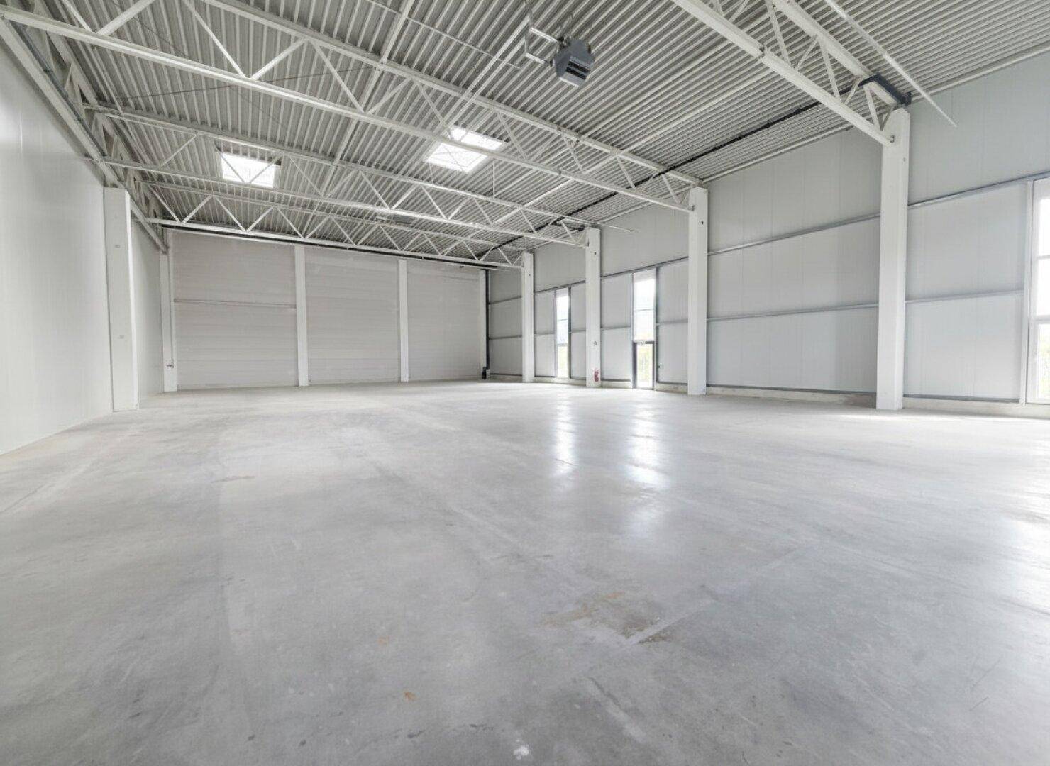 Helle, geräumige Lagerhalle mit Betonboden, hohen Decken und mehreren Fenstern.