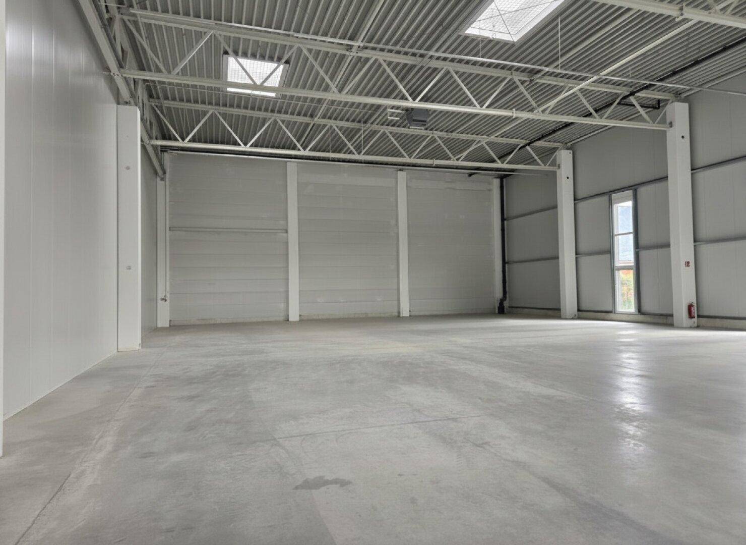 Innenansicht einer modernen Lagerhalle mit hohen Decken, Betonboden und Rolltor.