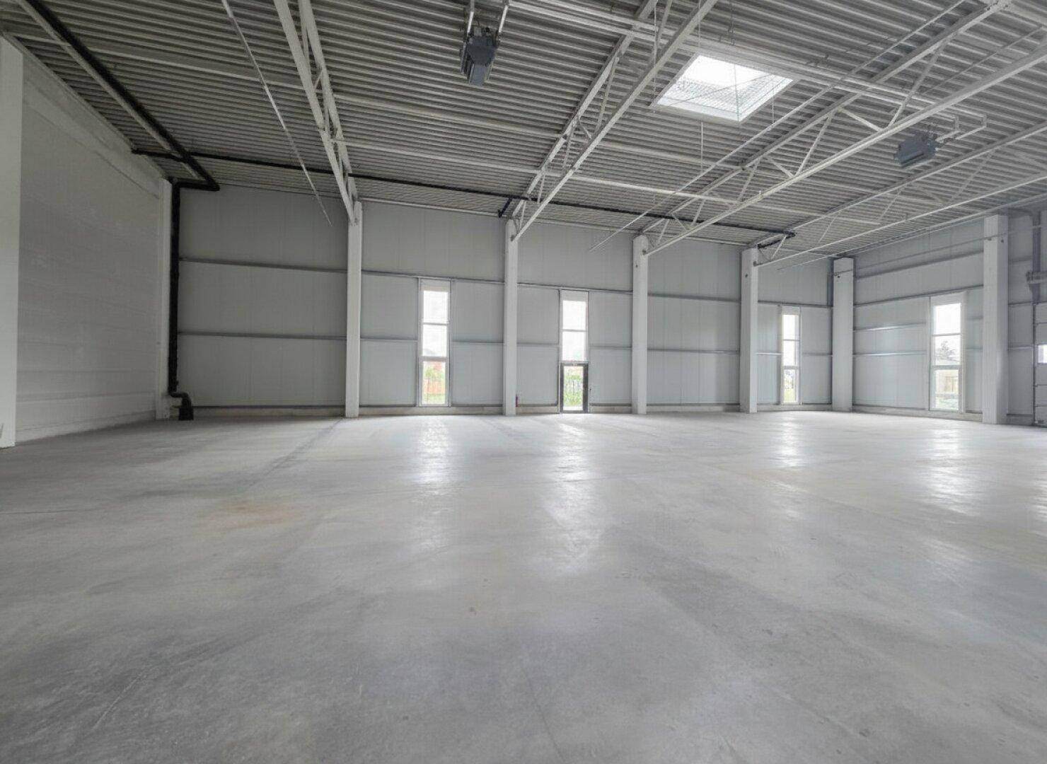 Weitläufige, ungenutzte Lagerfläche mit hohen Decken, Betonboden und natürlicher Beleuchtung.