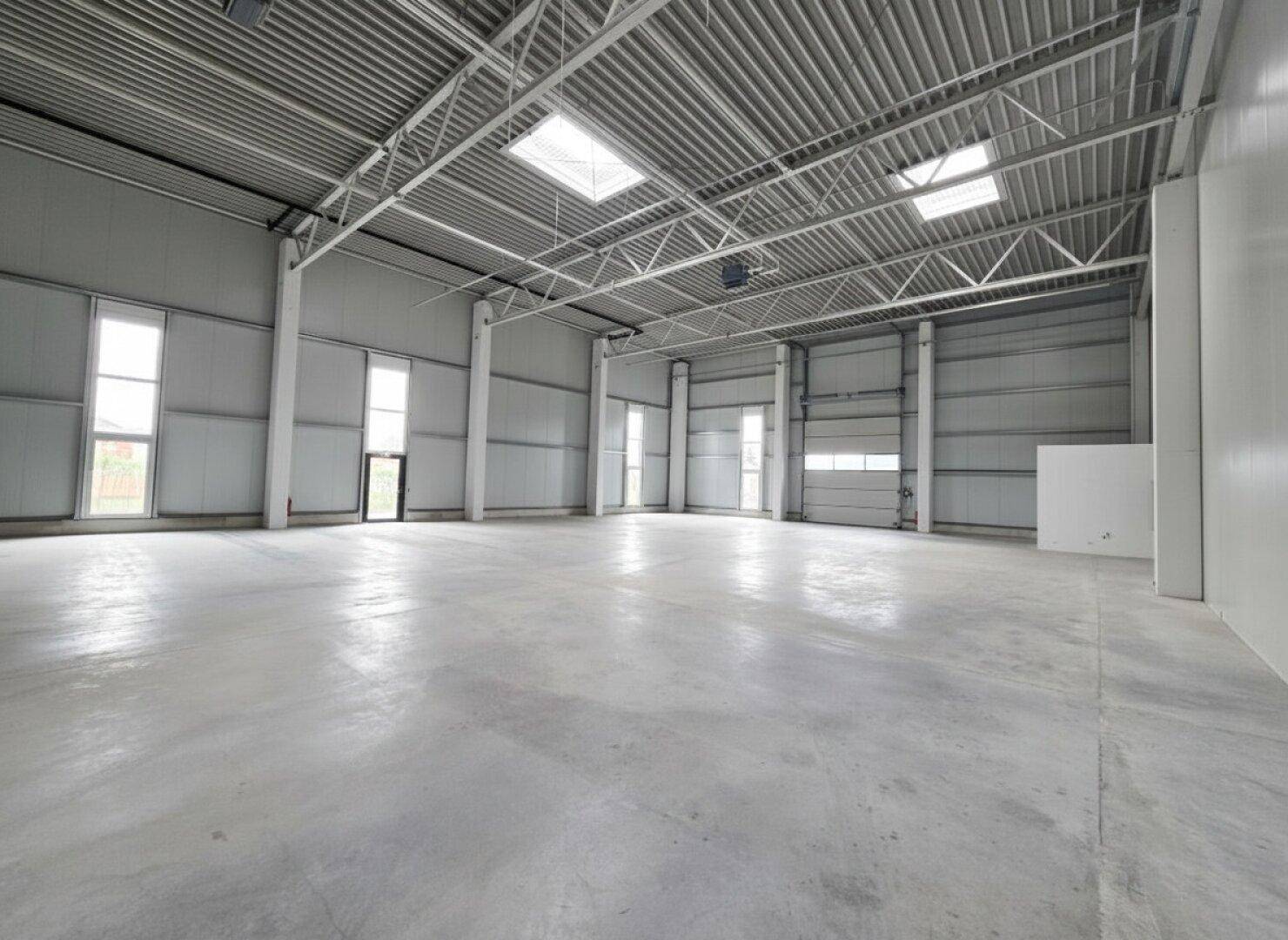 Geräumige, leere Lagerhalle mit hohen Decken, Betonboden und großen Fenstern für viel Tageslicht.