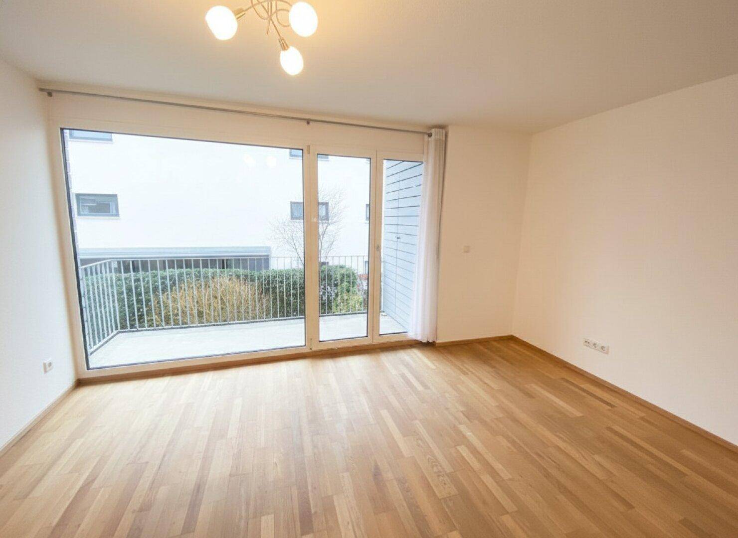 Helles Wohnzimmer mit Holzboden und großem Zugang zu einem Balkon, der viel Licht hereinlässt.