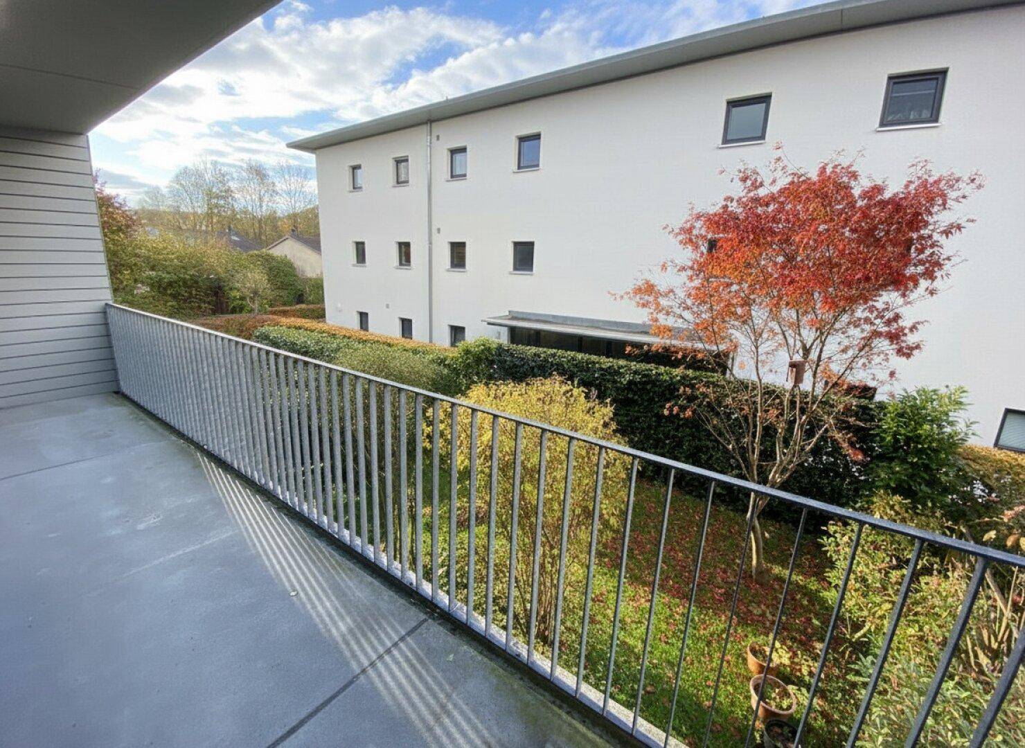 Balkon mit Blick auf die grüne Umgebung und das moderne Gebäude unter blauem Himmel.