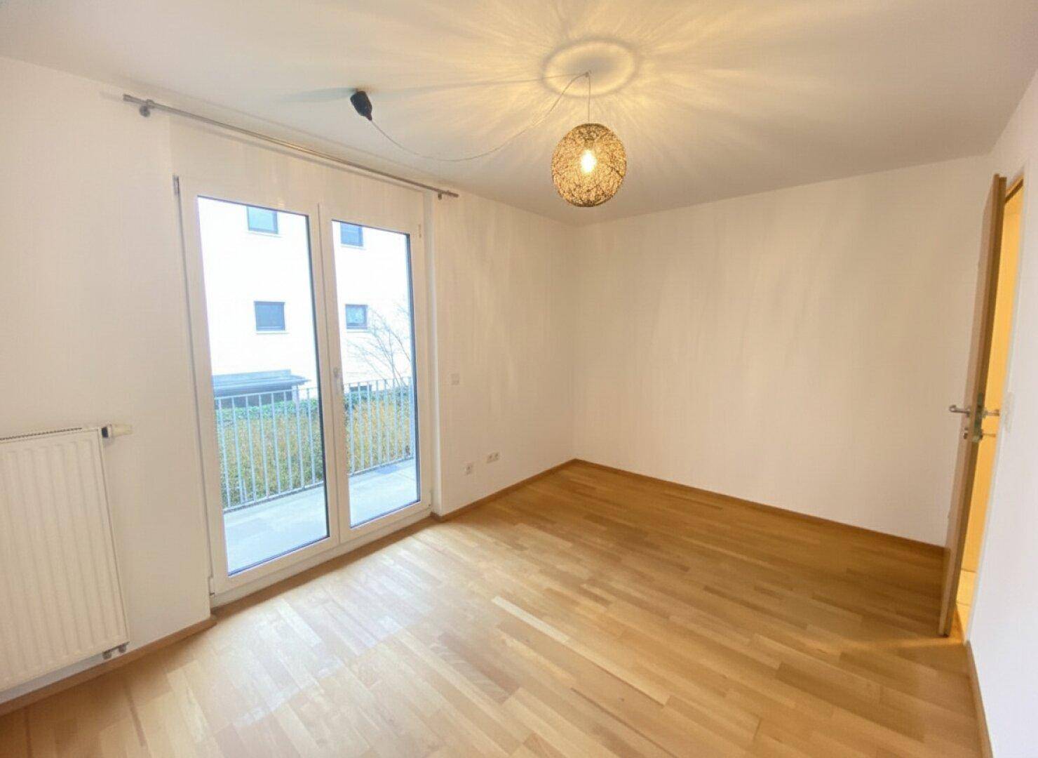 Helles Schlafzimmer mit Holzboden und Balkontür, gut beleuchtet durch Tageslicht.