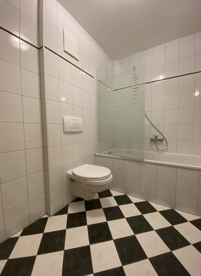 Badezimmer mit WC, Badewanne und markanten schwarz-weiß karierten Bodenfliesen.