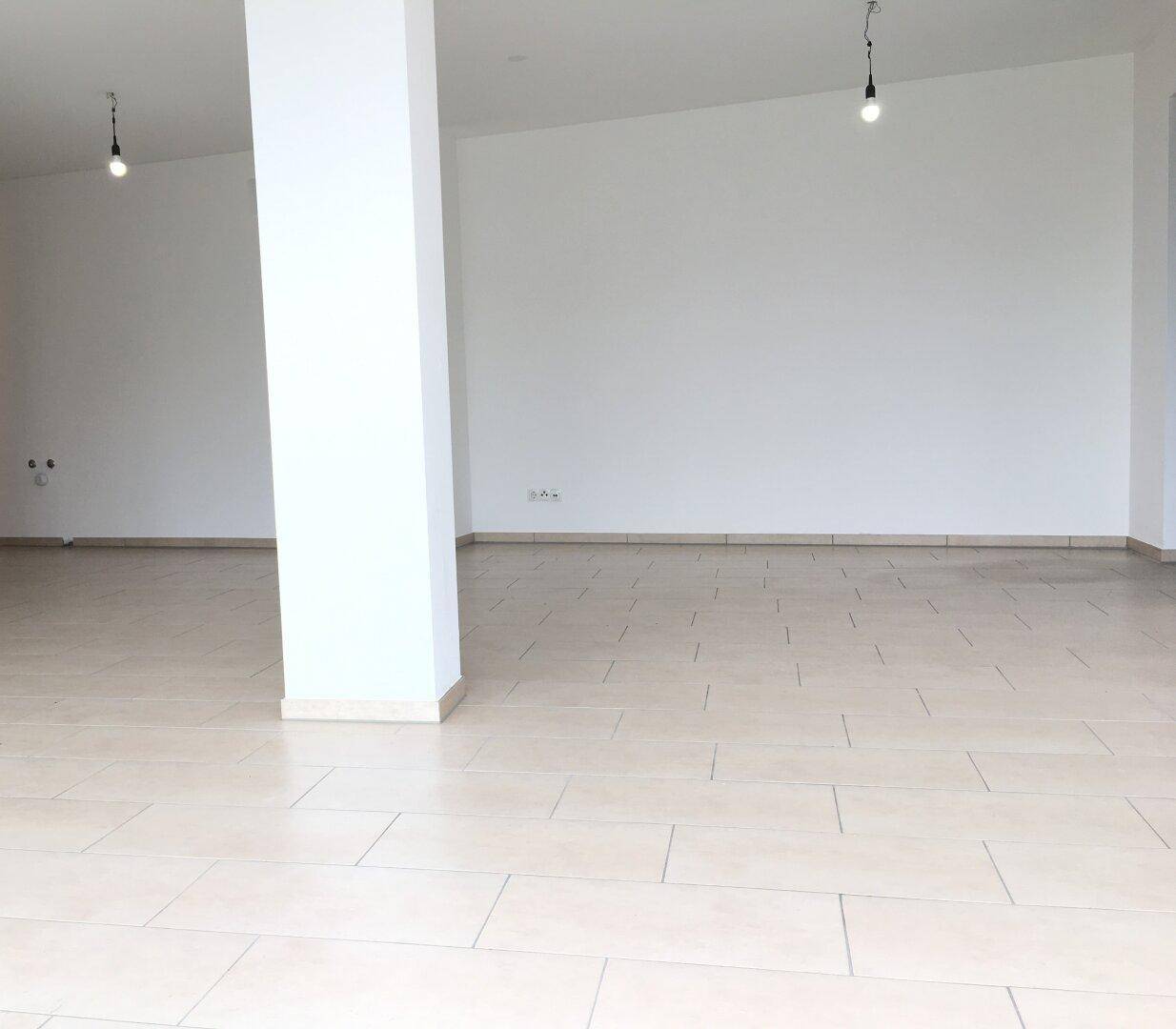 Weitläufiger, leerer Raum mit hellen Fliesenböden und weißen Wänden, bereit zur Gestaltung.