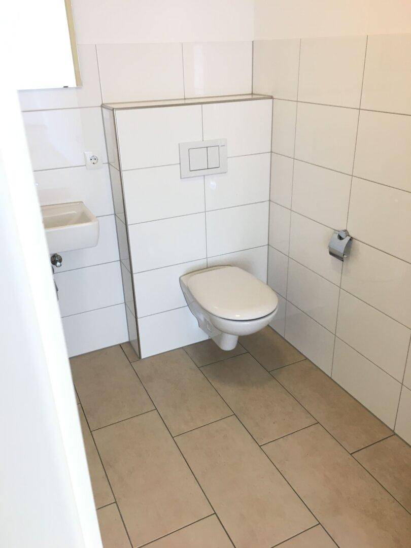 Modernes Gäste-WC mit wandhängender Toilette, kleinem Waschbecken und weißen Fliesen.