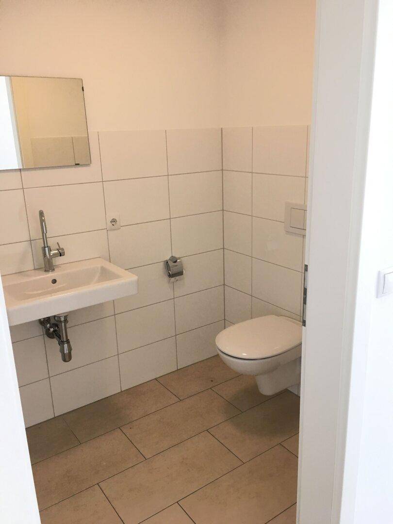 Helles Gäste-WC mit Waschbecken, Spiegel und wandhängender Toilette in modernem Design.