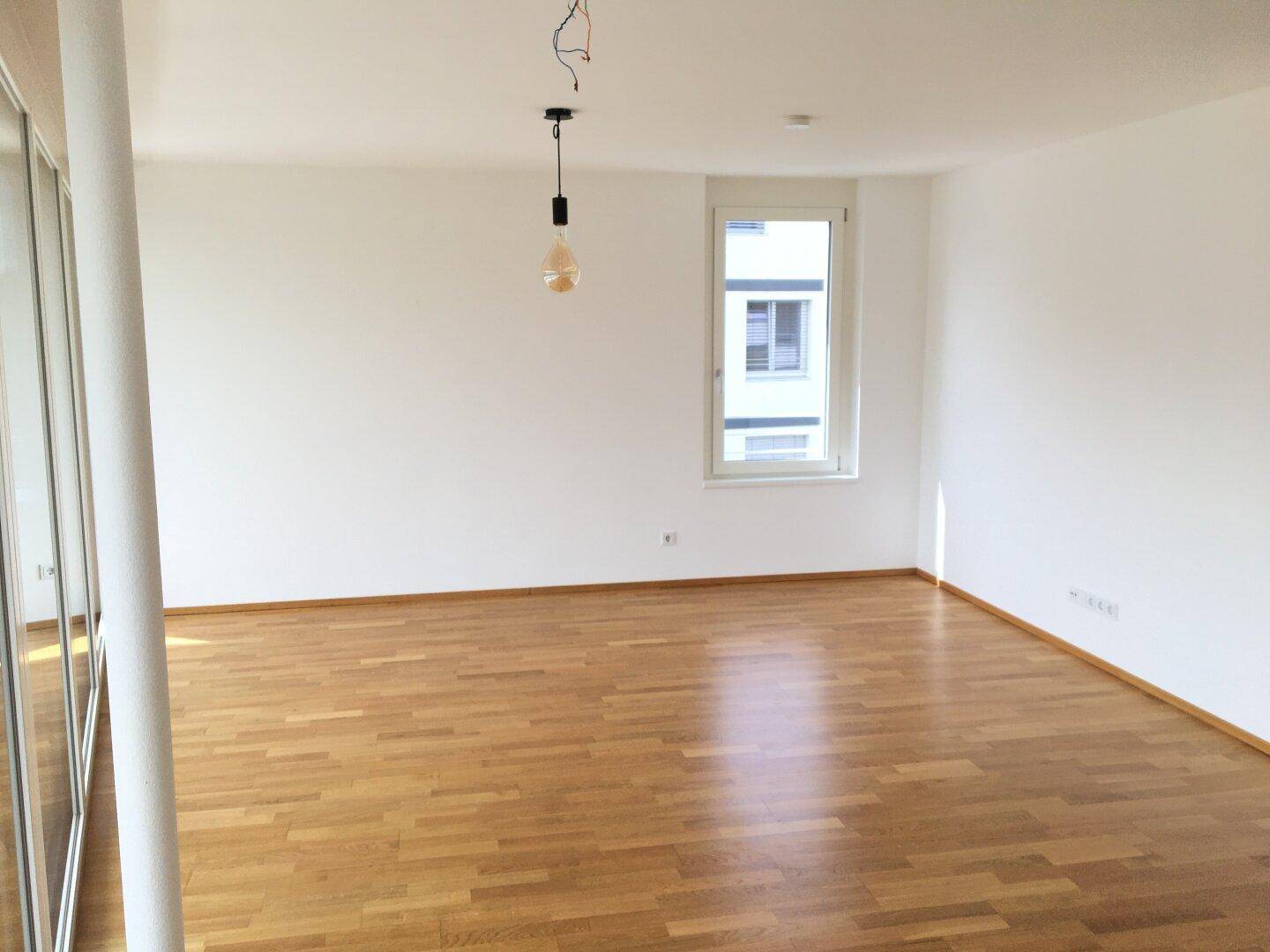 Helles, leeres Zimmer mit Holzboden und einem Fenster, bereit zur individuellen Gestaltung.