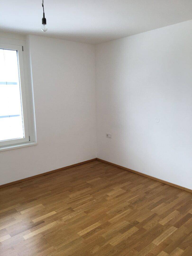 Unmöbliertes Zimmer mit Holzboden und einem Fenster, das viel Tageslicht hereinlässt.