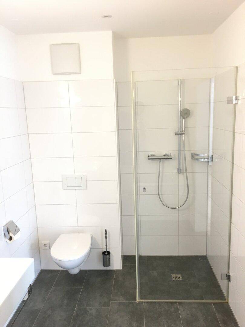 Modernes Badezimmer mit weiß gefliesten Wänden, dunklem Boden und einer ebenerdigen Dusche.