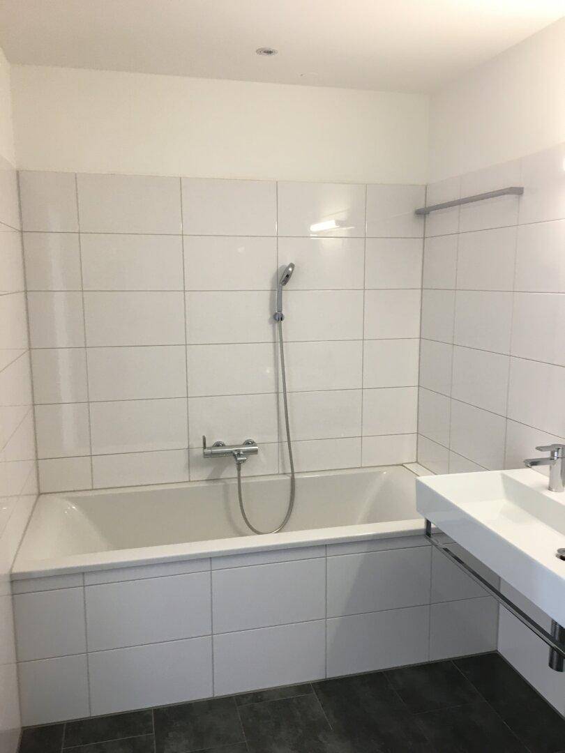 Badezimmer mit Badewanne, weißer Wandfliesen und einem modernen Waschbecken.
