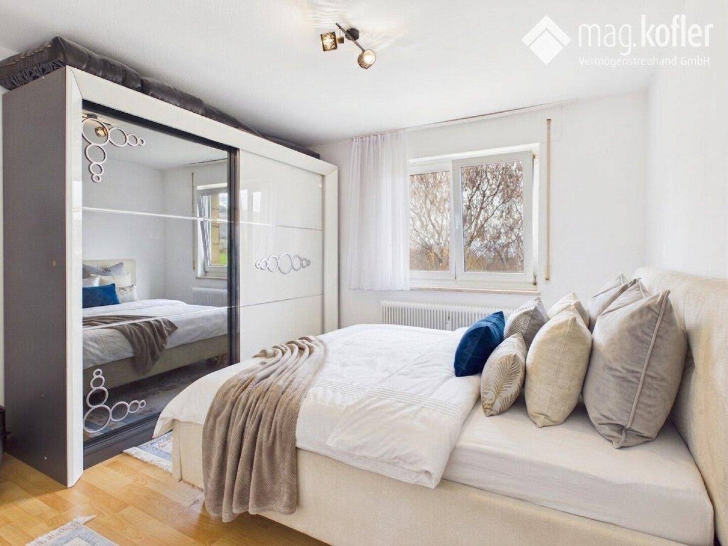 Helles Schlafzimmer mit großem Bett, Spiegelschrank und Blick ins Grüne durch das Fenster.