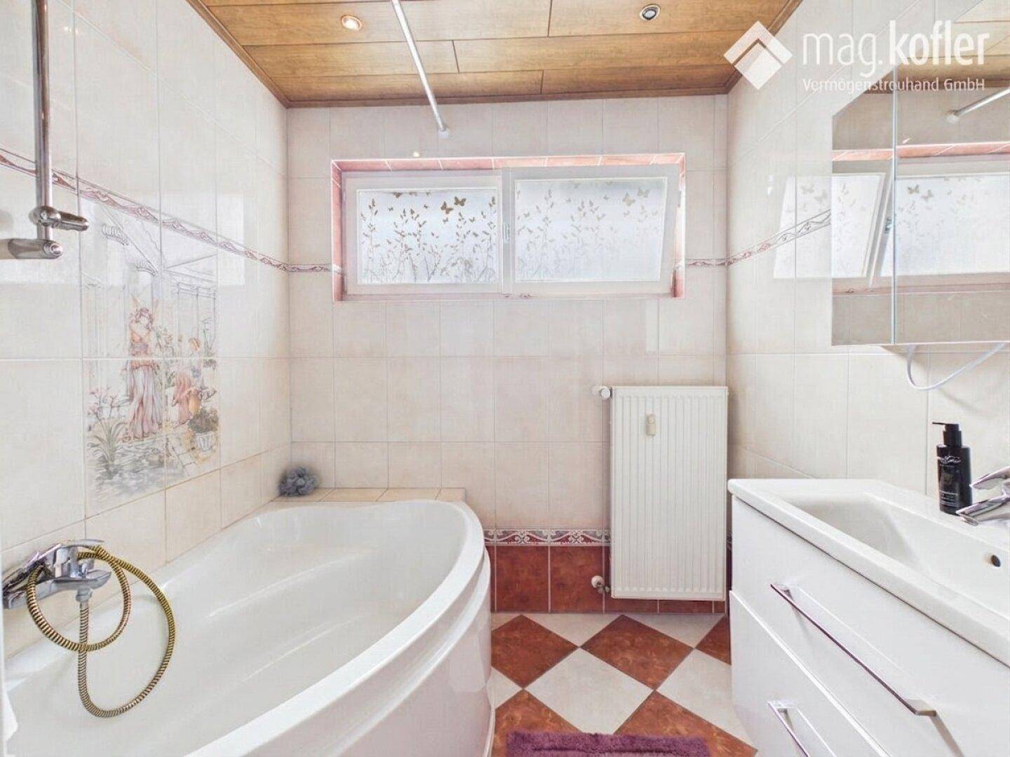 Badezimmer mit Badewanne, Waschbecken und Fenster, ausgestattet mit Fliesenboden und Holzdecke.