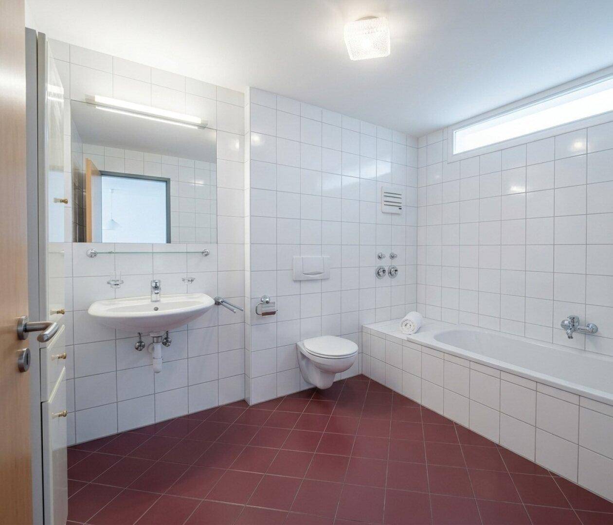 Gefliestes Badezimmer mit Badewanne, Waschbecken und Toilette in hellem Design.
