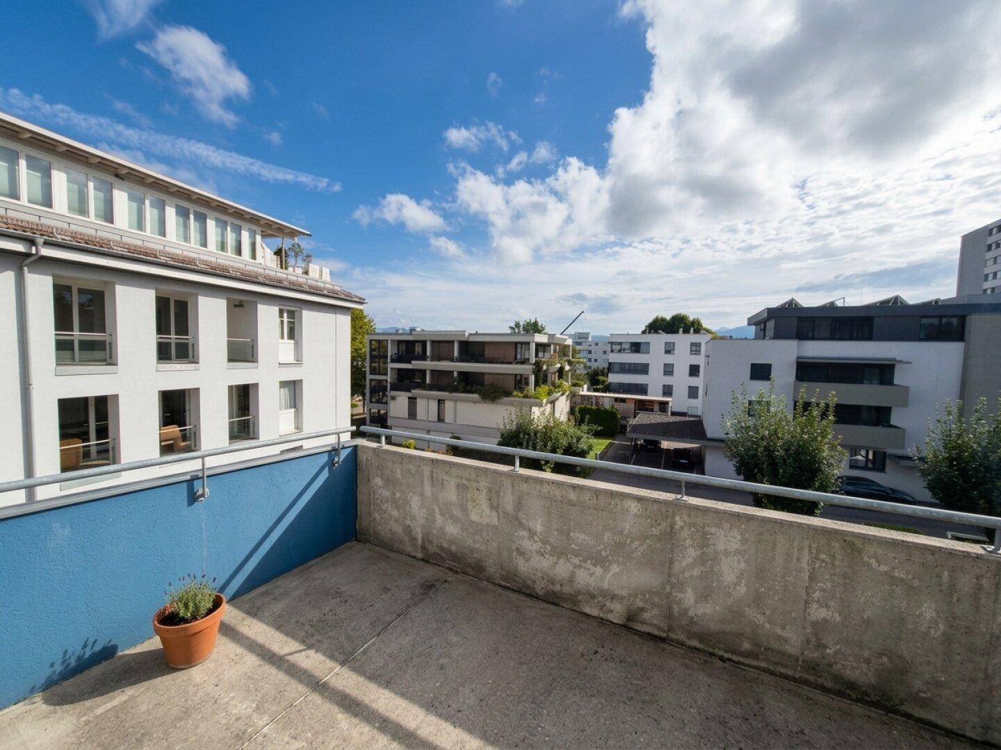 Betonbalkon mit Blick auf umliegende moderne Gebäude und den blauen Himmel.