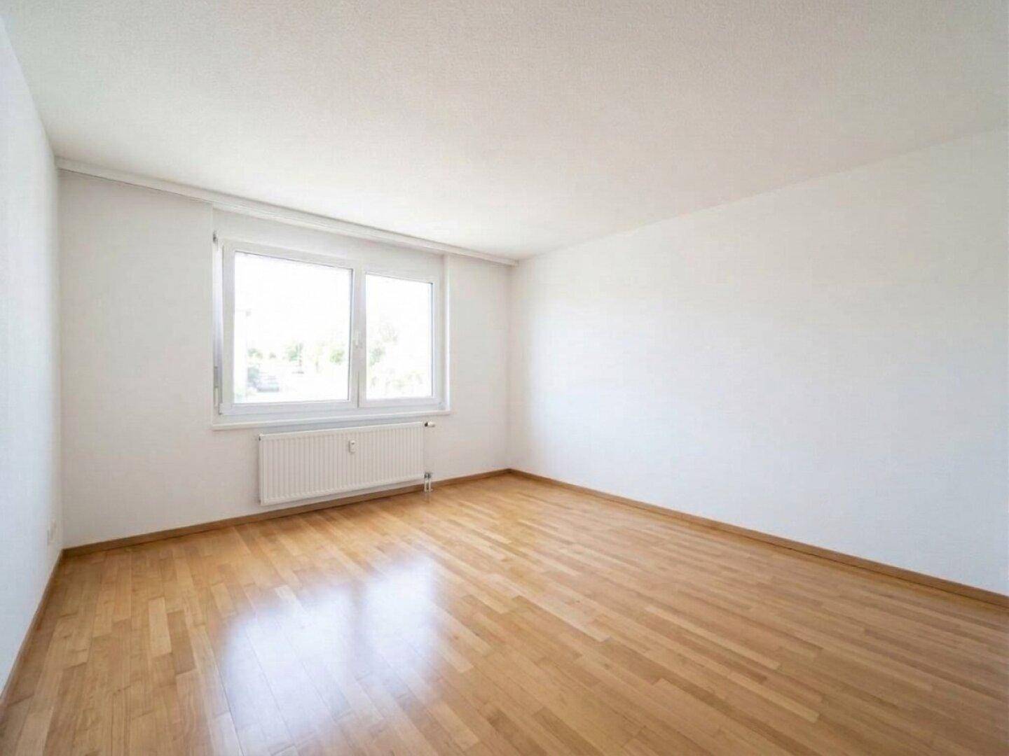 Helles Schlafzimmer mit Parkettboden und einem großen Fenster für ausreichend Tageslicht.
