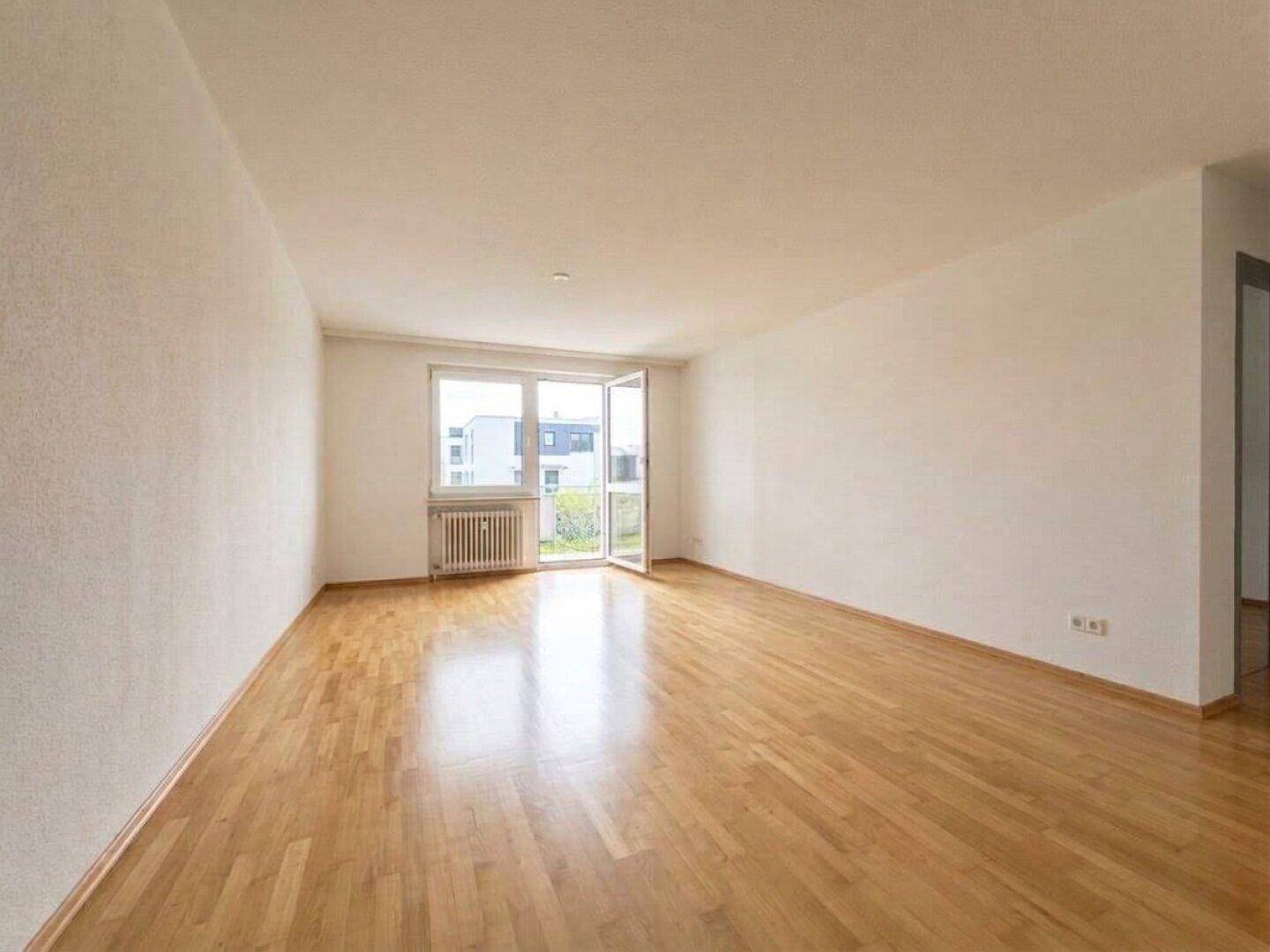 Heller Wohnraum mit Holzparkett und großem Fenster, das viel Tageslicht hereinlässt.