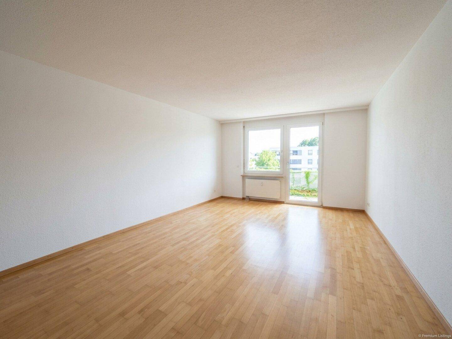 Geräumiger, heller Raum mit Parkettboden und Zugang zu einem Balkon oder einer Terrasse.