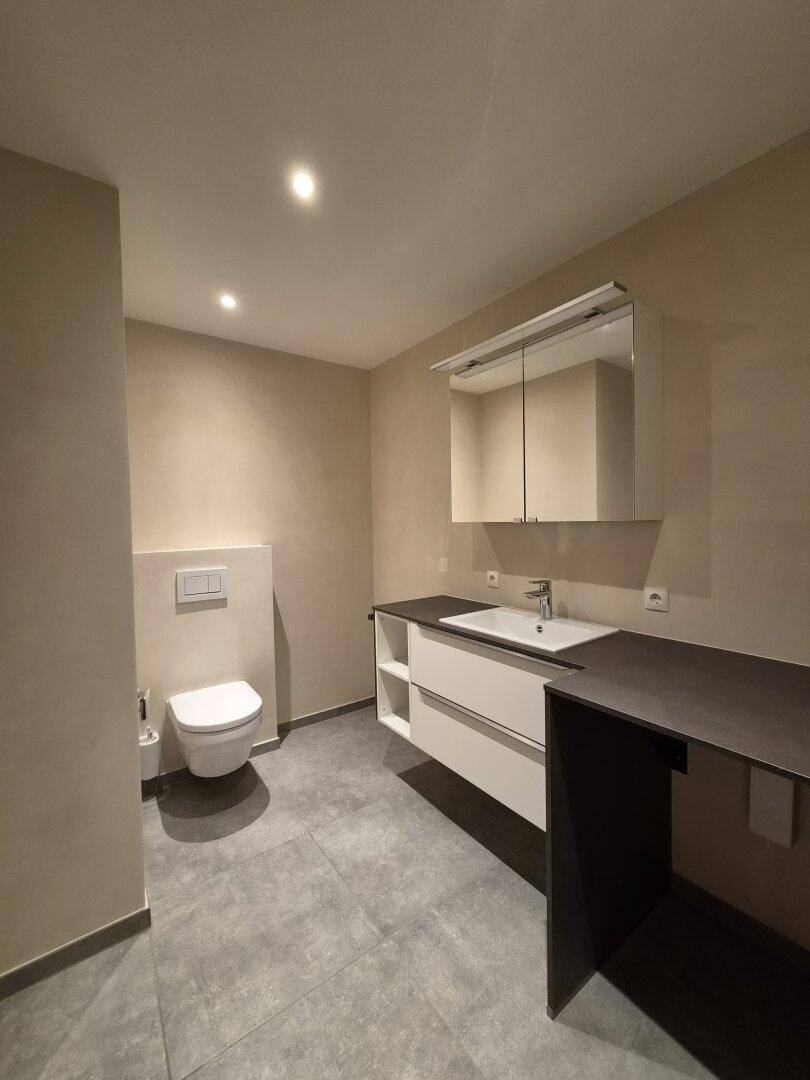 Modernes Badezimmer mit Wand-WC, Einzelwaschbecken und Spiegelschrank, in neutralen Farbtönen gehalten.