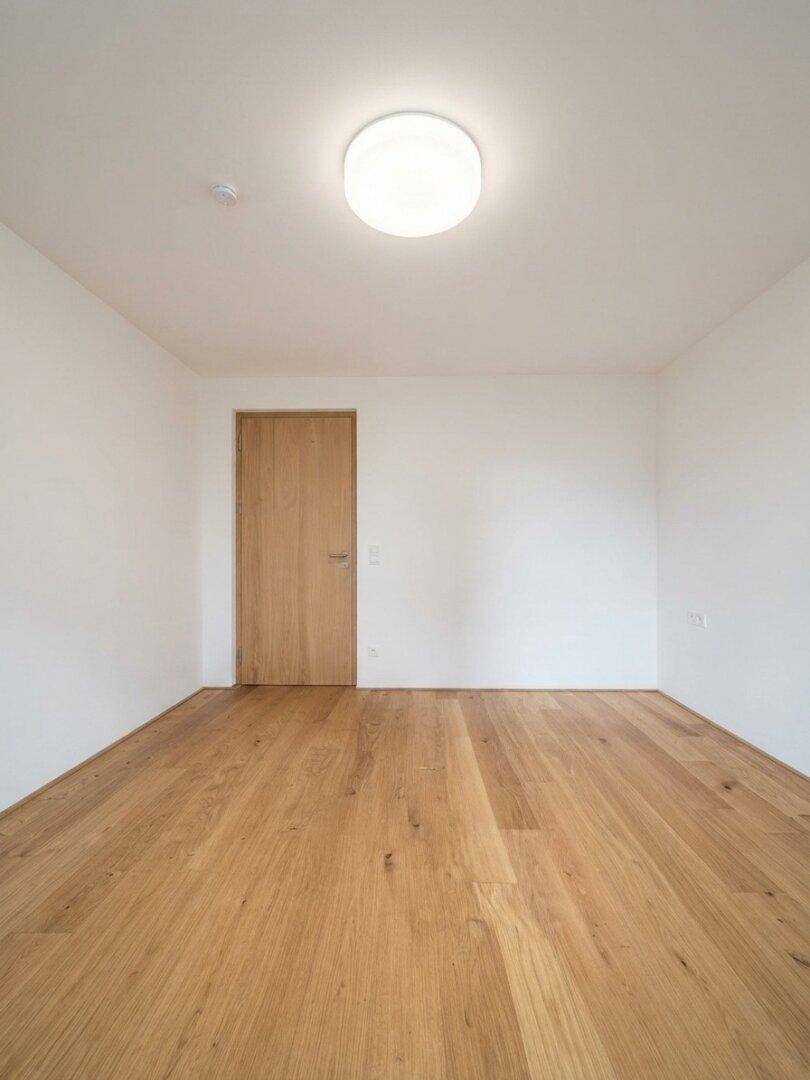 Schlichter, heller Raum mit Holzboden und einer modernen Holztür, bereit zur individuellen Gestaltung.