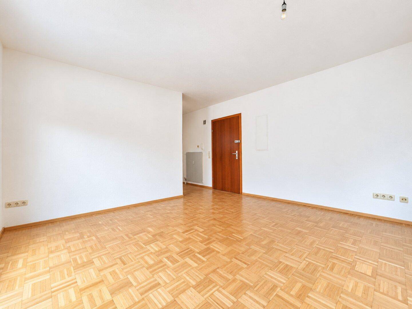 Leerer Wohnbereich mit Parkettboden und einer Holztür, bereit für individuelle Gestaltung.