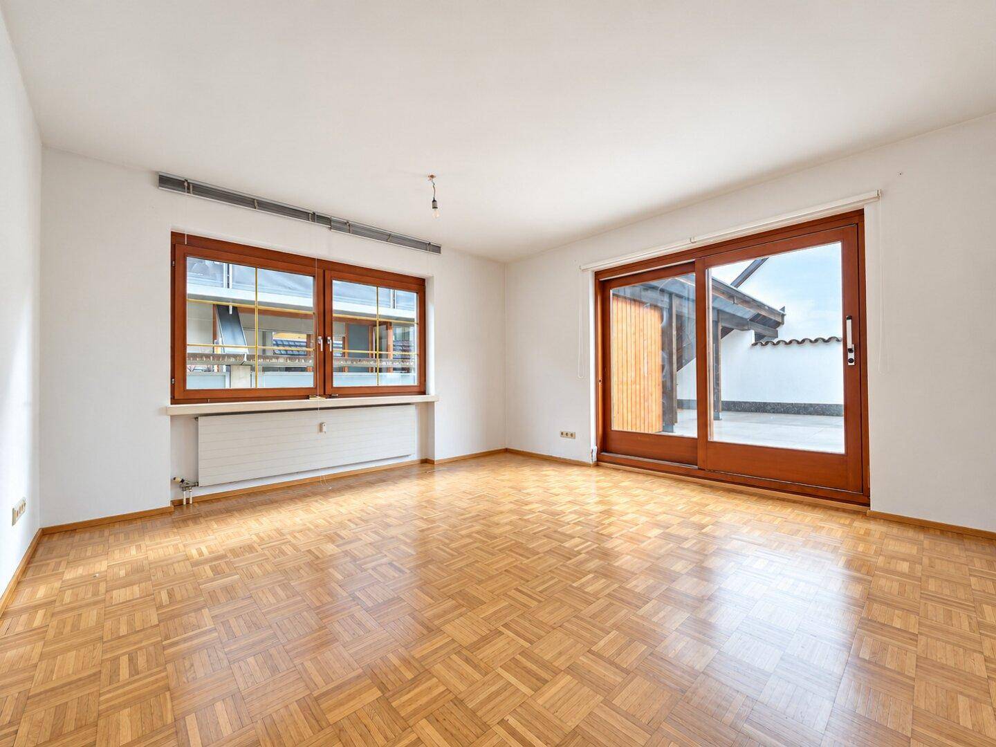 Geräumiges, helles Zimmer mit Parkettboden, großen Fenstern und Zugang zu einem Außenbereich.