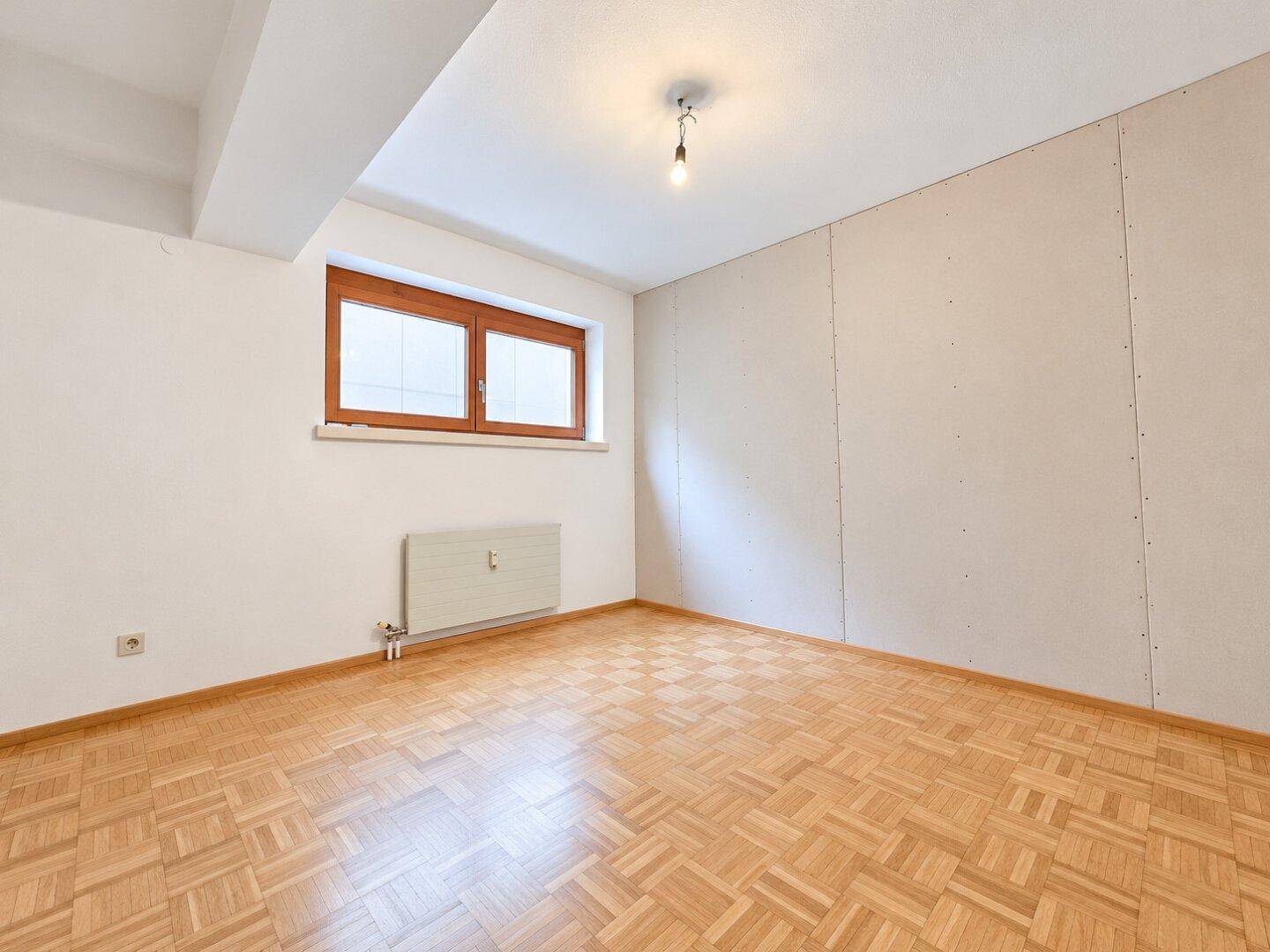Helles Zimmer mit Parkettboden, Fenster und Heizkörper, bereit für individuelle Nutzung.