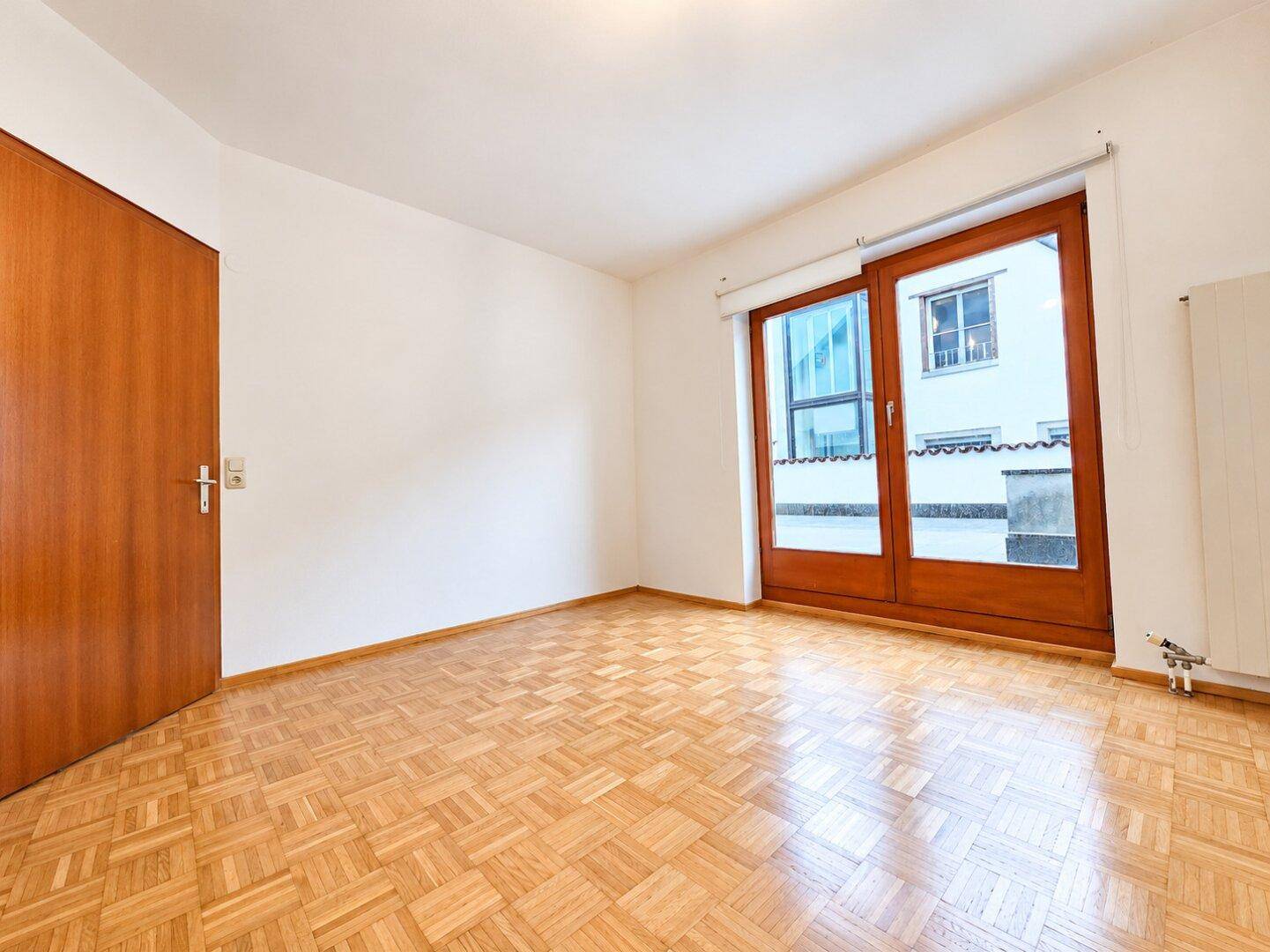 Helles Zimmer mit Parkettboden, Holztür und Zugang zu einem Außenbereich durch eine Schiebetür.