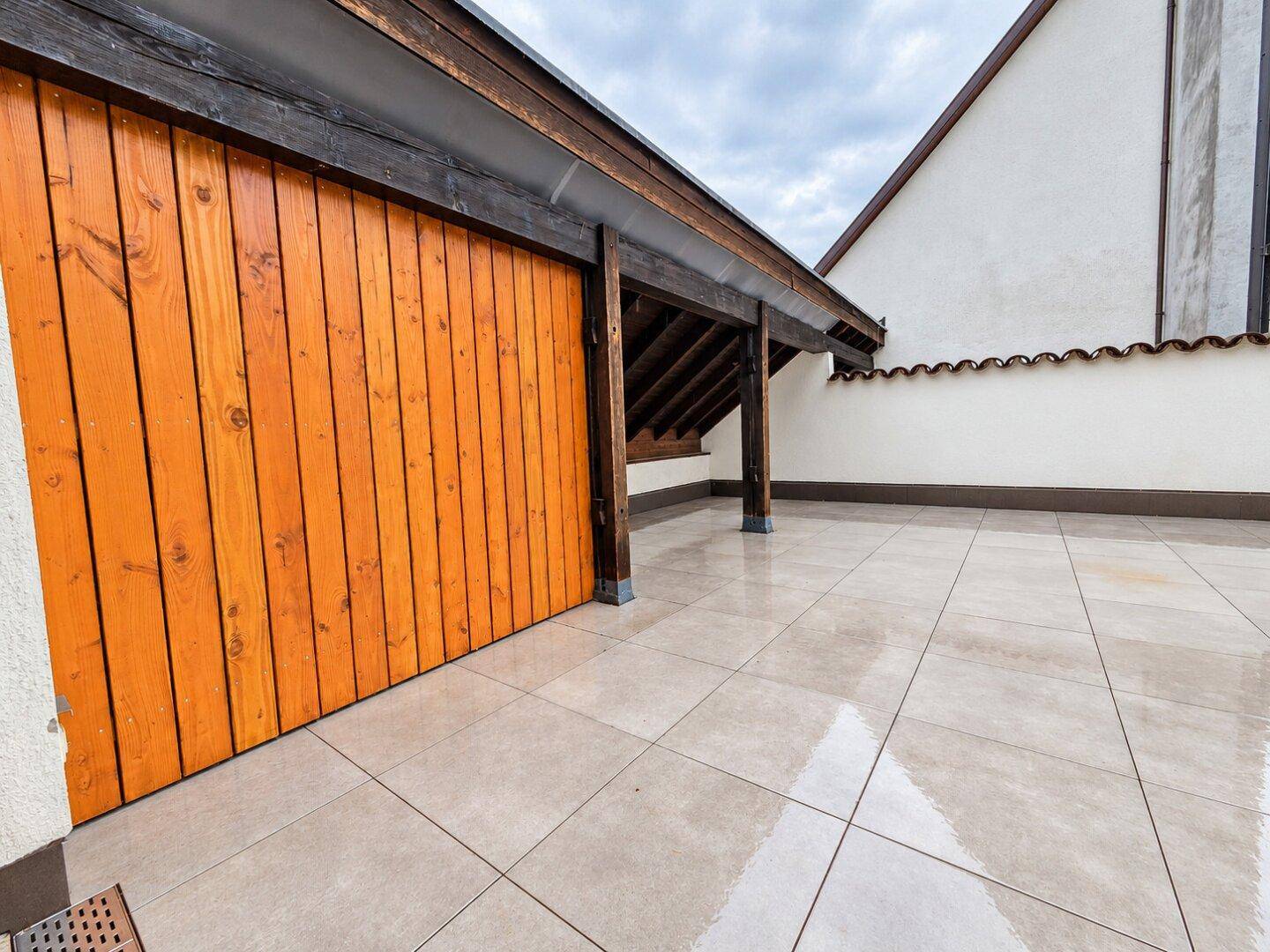 Weitläufige, geflieste Terrasse mit Holzelementen und Blick auf die umliegenden Gebäude.