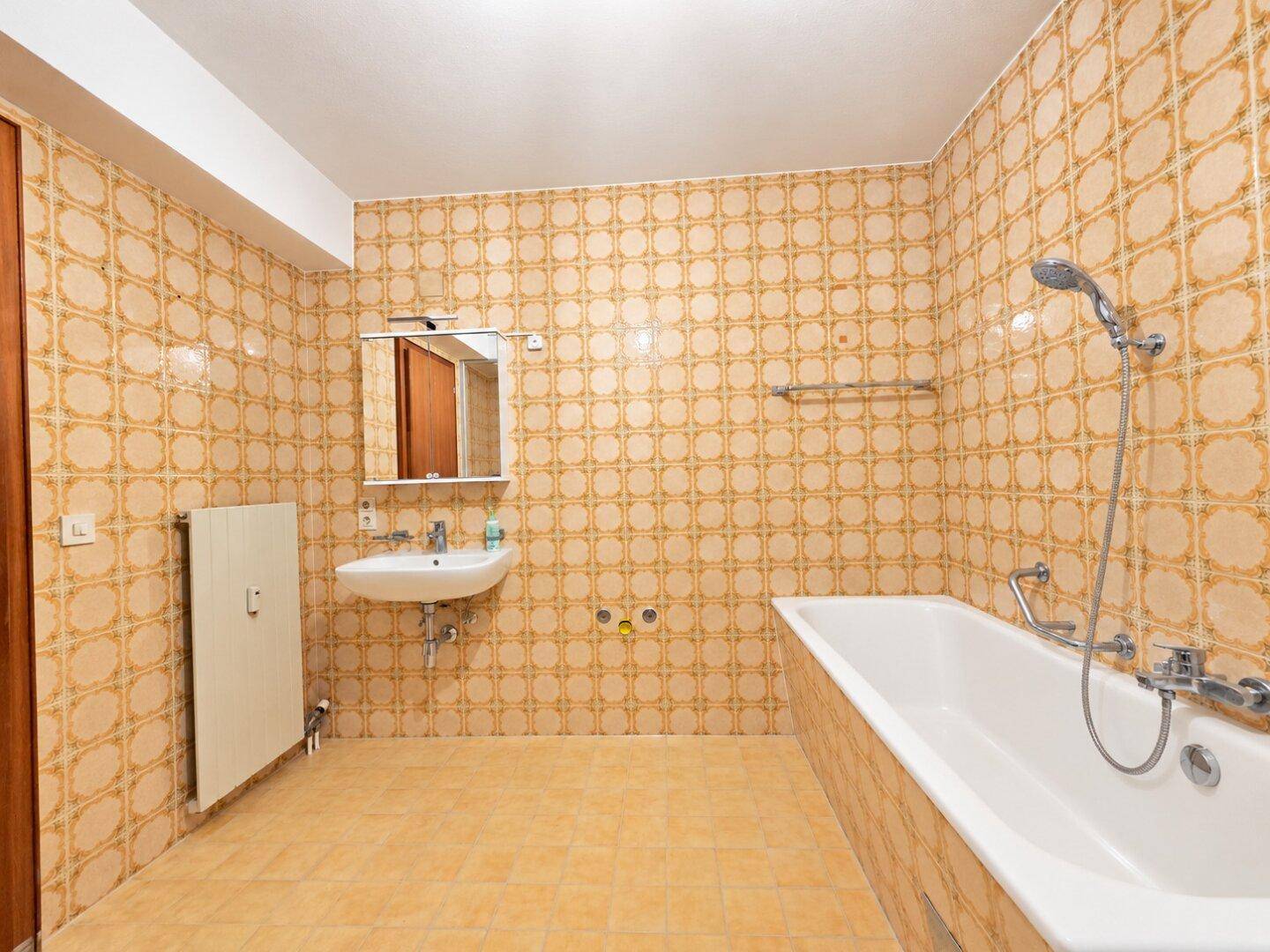 Badezimmer mit Badewanne, Waschbecken und gemusterten Fliesen im Retro-Stil.