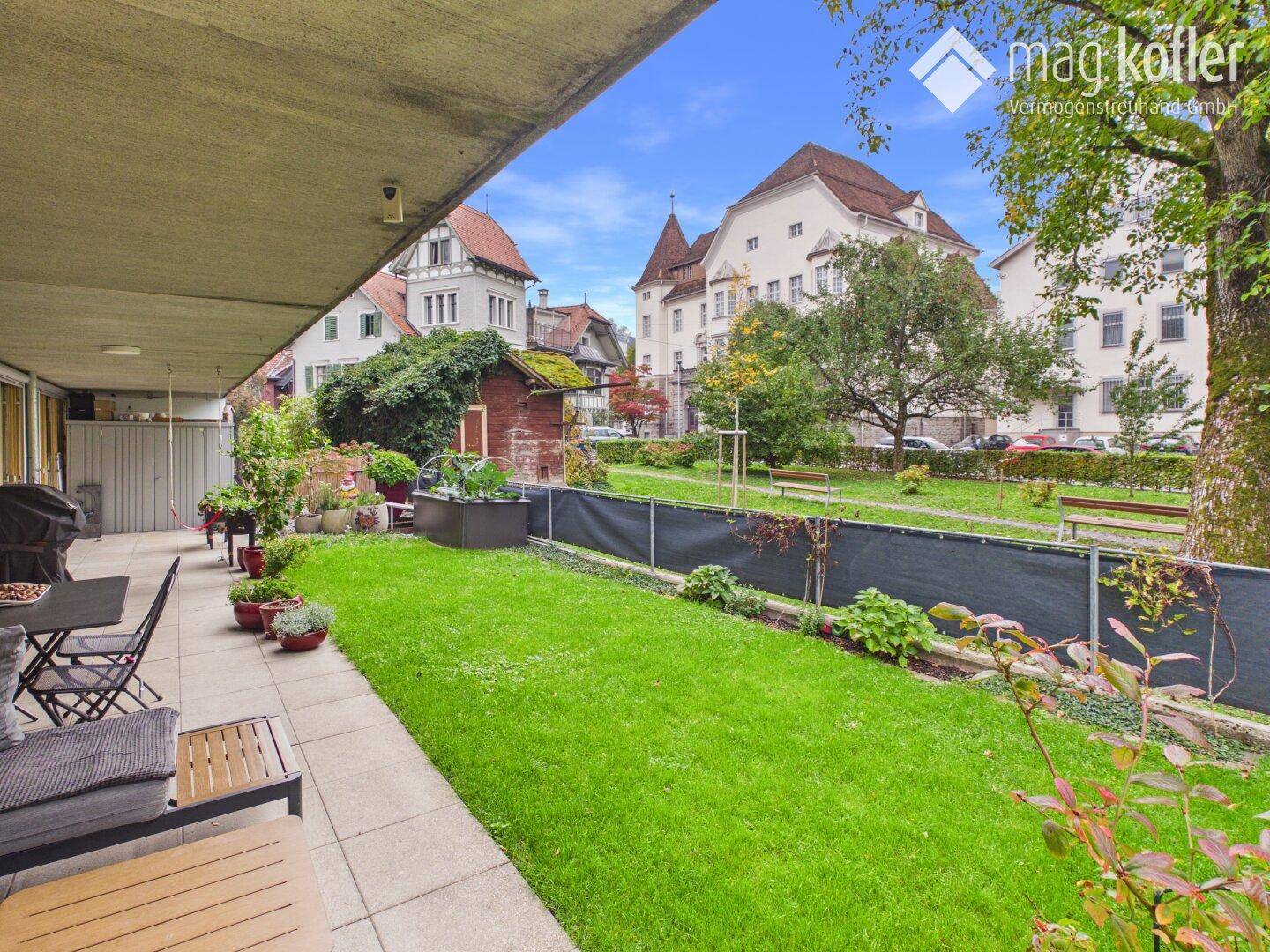 Gepflegter Gartenbereich mit Rasenfläche, Terrasse und Blick auf die umliegenden Gebäude.