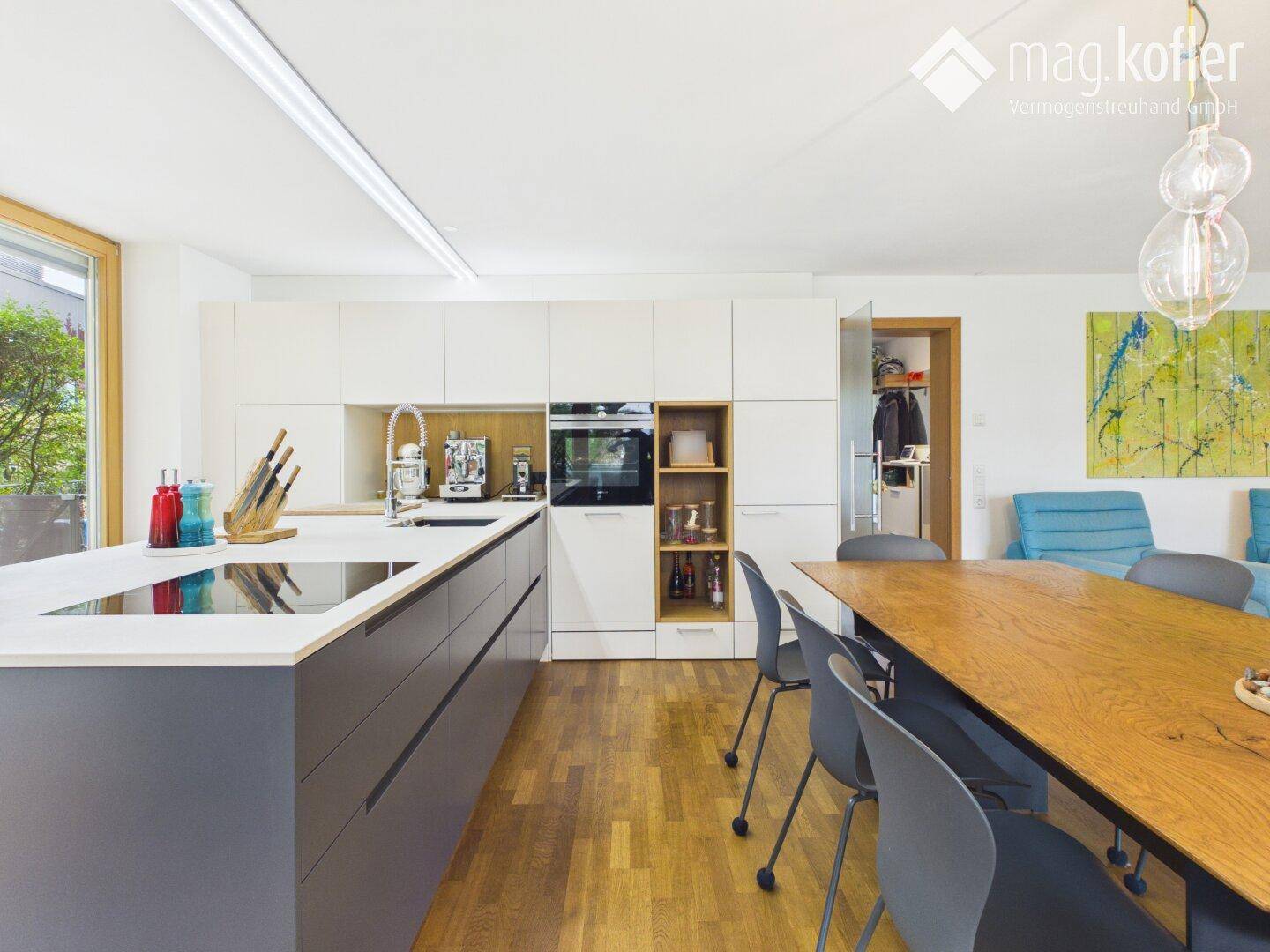 Moderne Einbauküche mit weißen und grauen Fronten, integrierten Geräten und Holzboden.