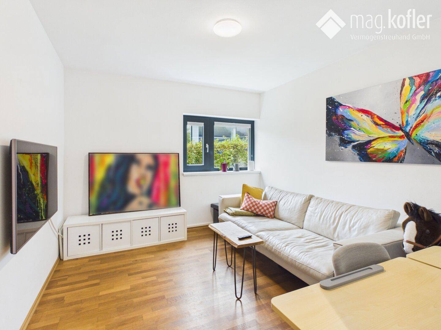 Helles Wohnzimmer mit Sofa, Fernseher und farbenfrohem Kunstwerk an der Wand.