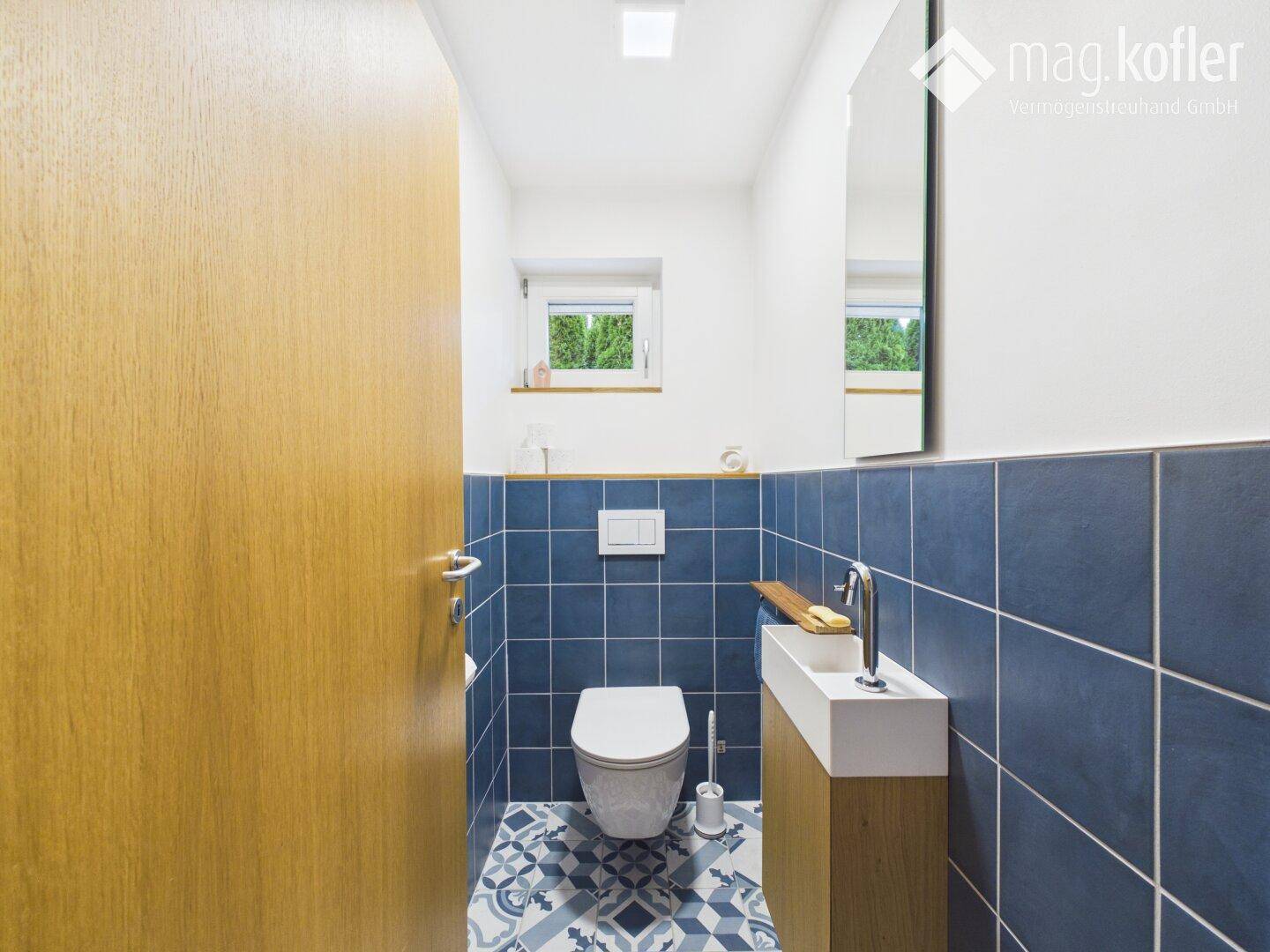 Separates WC mit modernem Waschbecken, Toilette und blauen Wandfliesen.