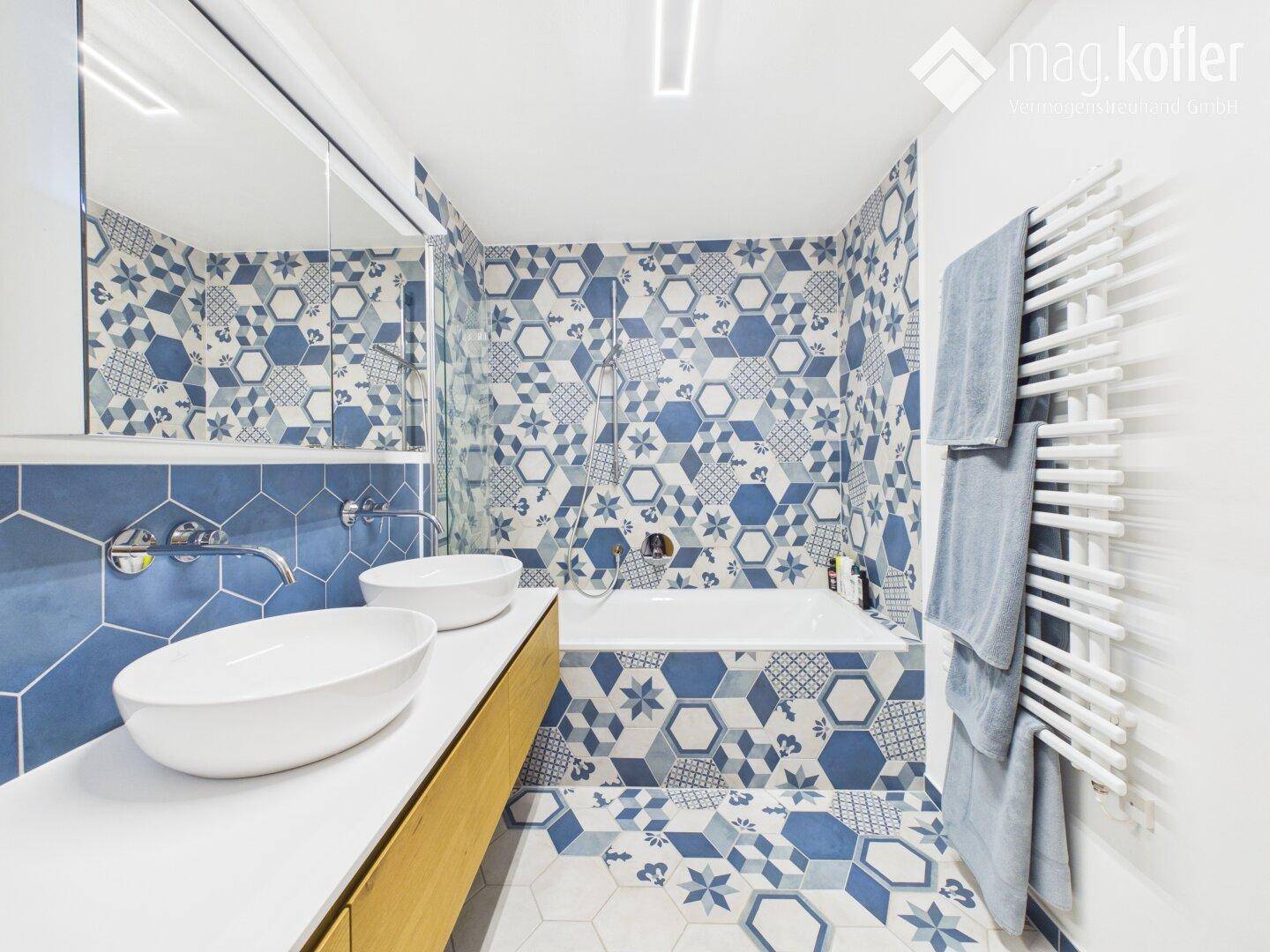 Stilvolles Badezimmer mit Badewanne, Doppelwaschbecken und gemusterten blauen Fliesen.