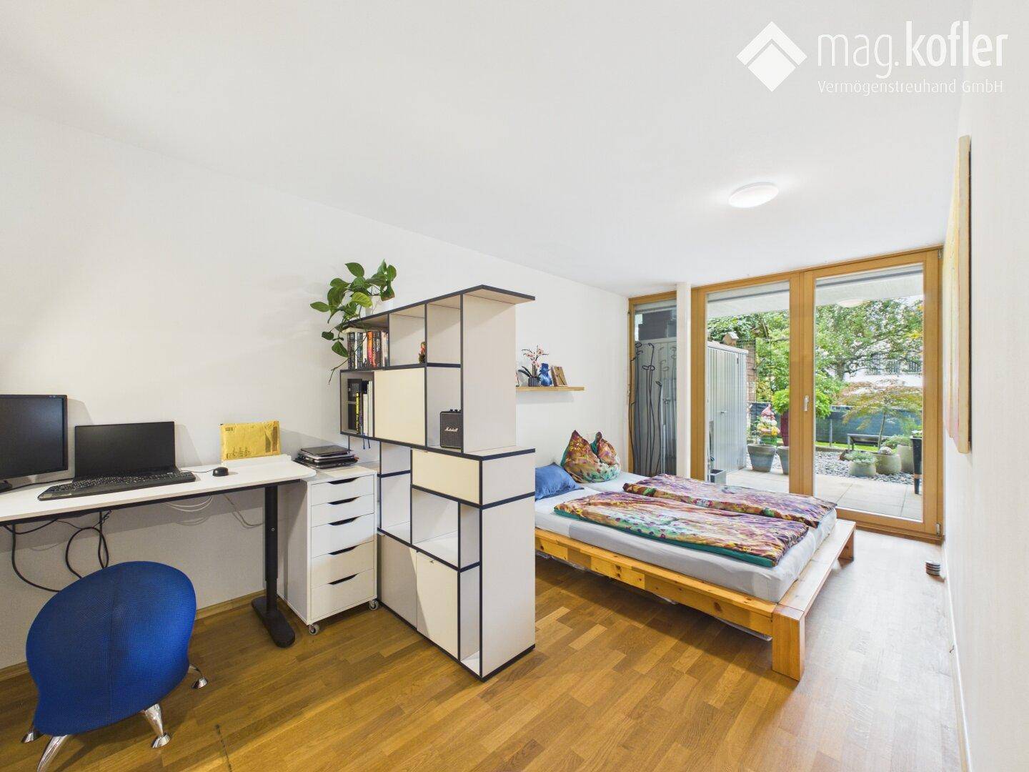 Schlafzimmer mit Holzbett, Schreibtisch und Zugang zur Terrasse.