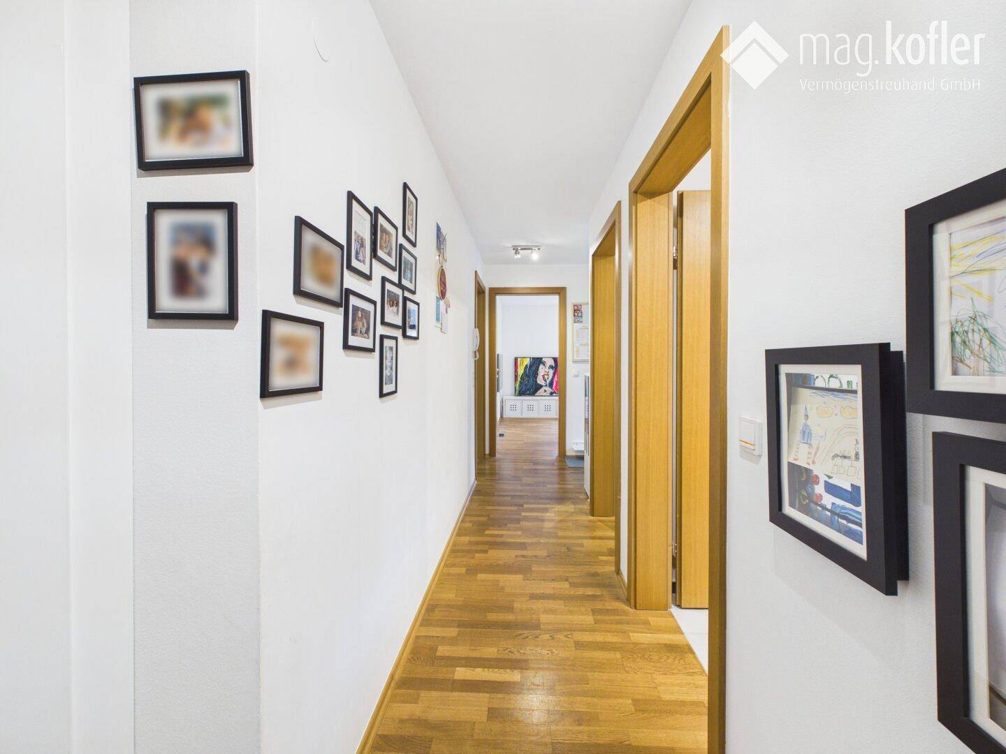 Langer Flur mit Holzboden und gerahmten Bildern an der Wand.