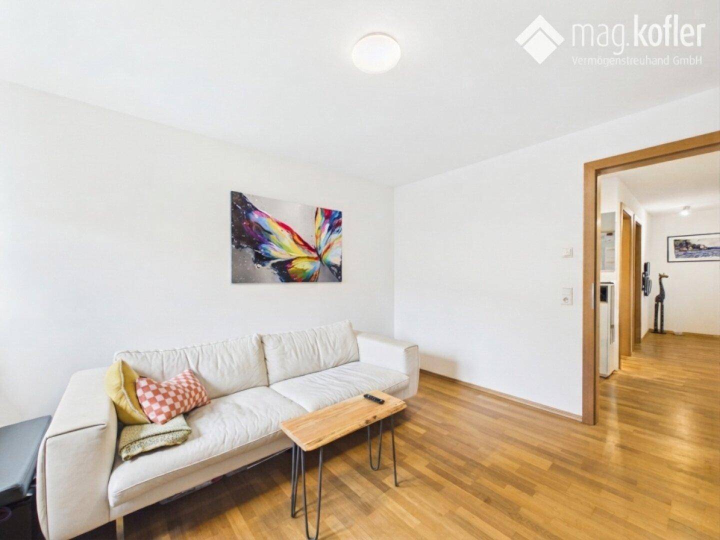 Gemütliches Wohnzimmer mit hellem Sofa, Holzboden und Zugang zum Flur.
